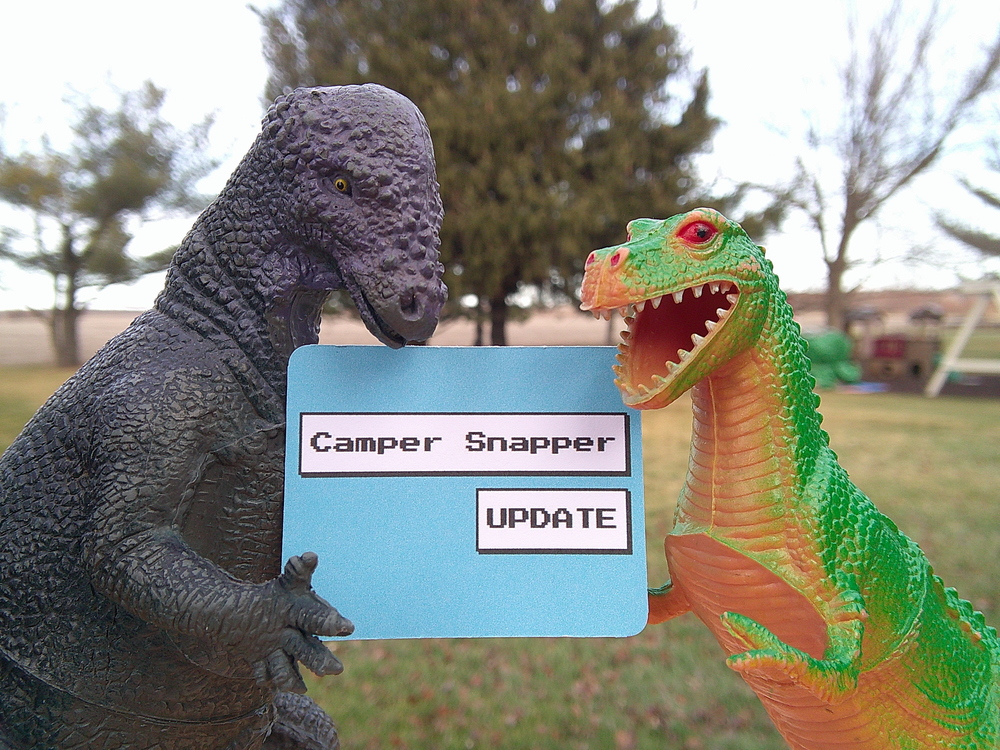 Two Happy Dinosaur toys holding a sign reading 'Camper Snapper Update'